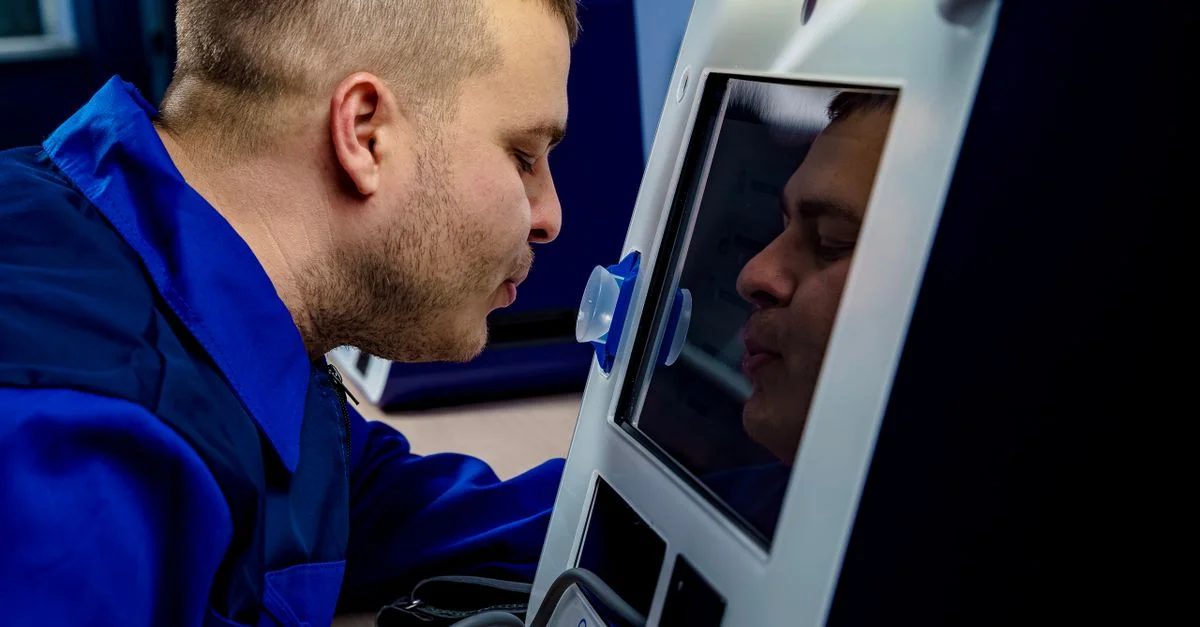 Un homme en uniforme bleu interagissant avec un appareil à écran tactile à l'intérieur.