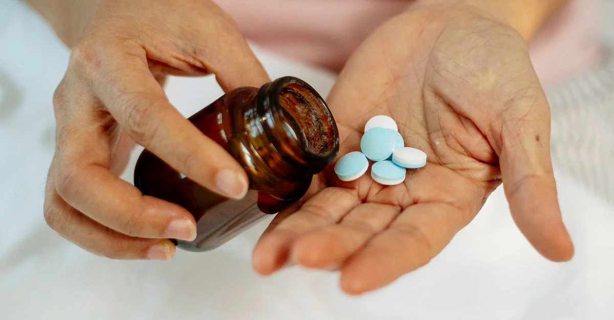 Gros plan sur des mains tenant des pilules provenant d'une bouteille en verre foncé, symbolisant les soins de santé.