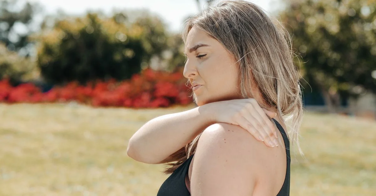 Femme en débardeur noir touchant son épaule en plein air. Concept de douleur à l'épaule et de relaxation.