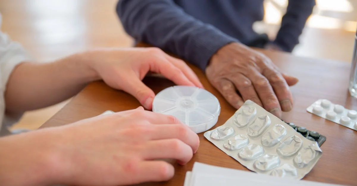 Gros plan sur des mains triant des médicaments et un organiseur de pilules sur une table en bois.
