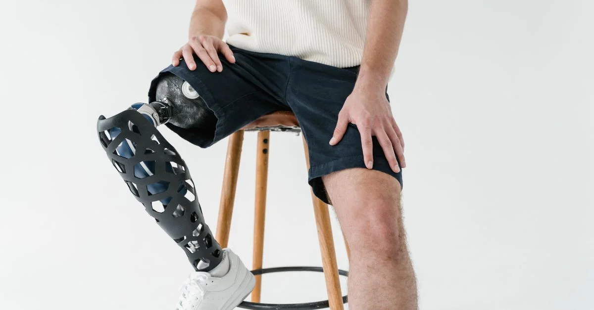 Homme adulte avec une jambe prothétique assis sur un tabouret en bois, vêtu de vêtements décontractés. Concept de handicap et de technologie.