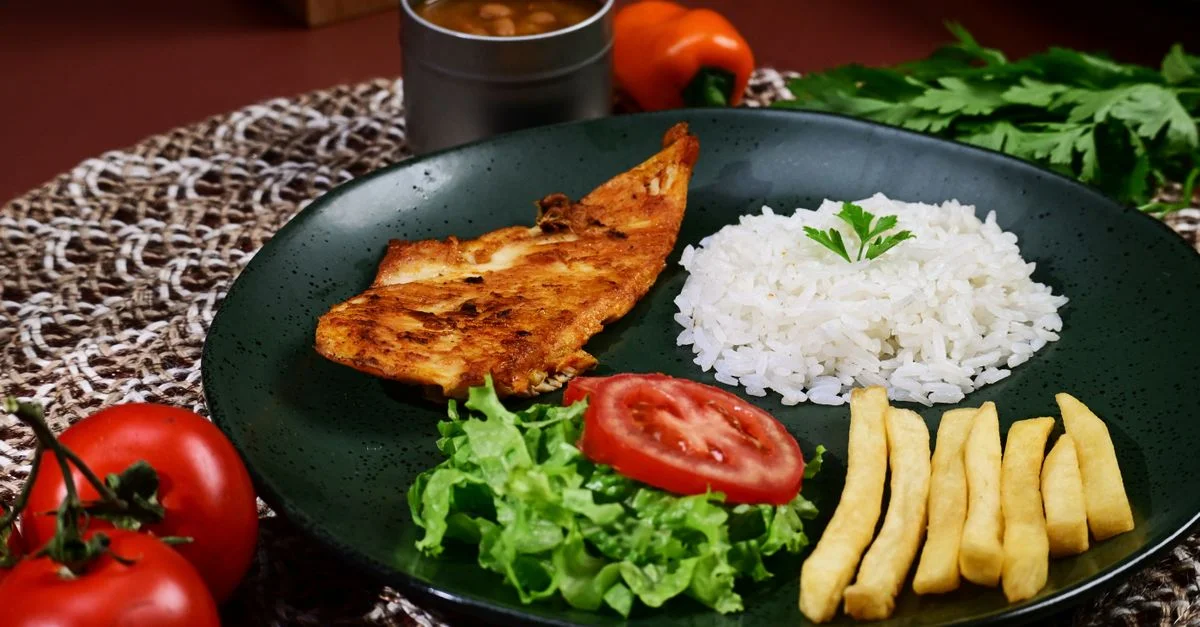 Une assiette colorée composée de blanc de poulet grillé, de riz blanc, de frites et de légumes frais.