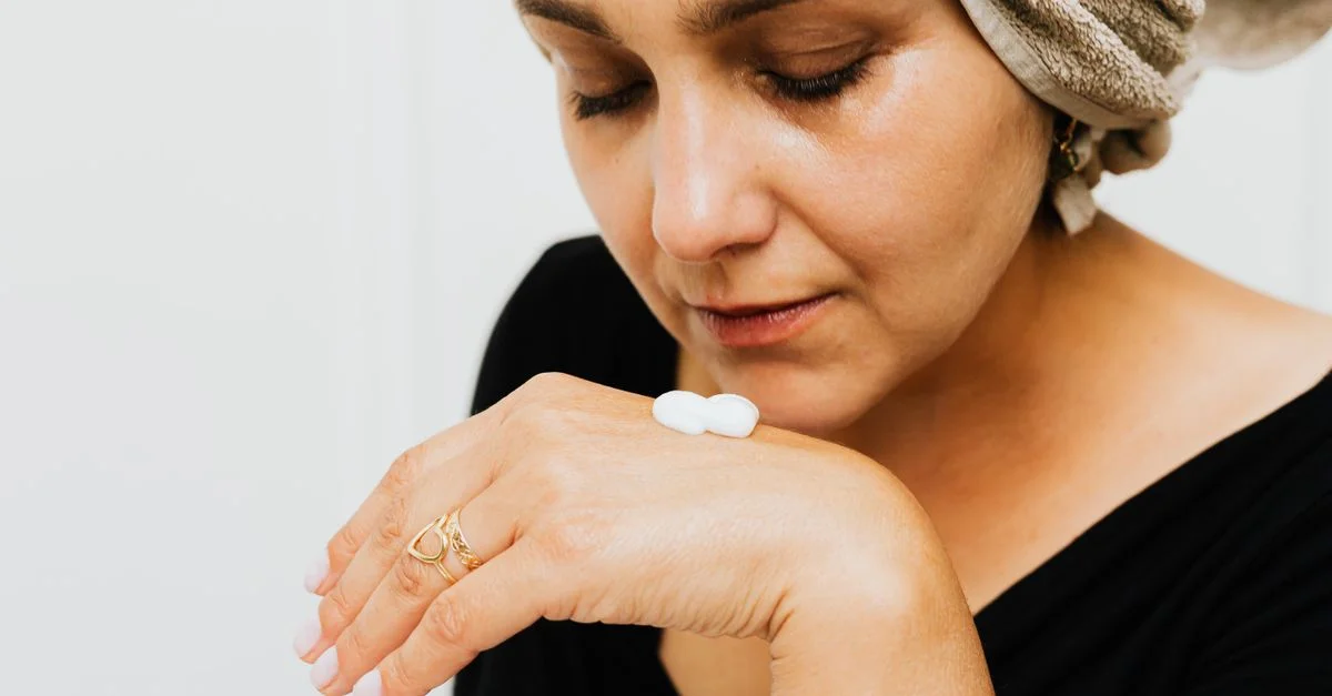 Gros plan d'une femme appliquant de la crème de soin sur sa main, promouvant les soins personnels.