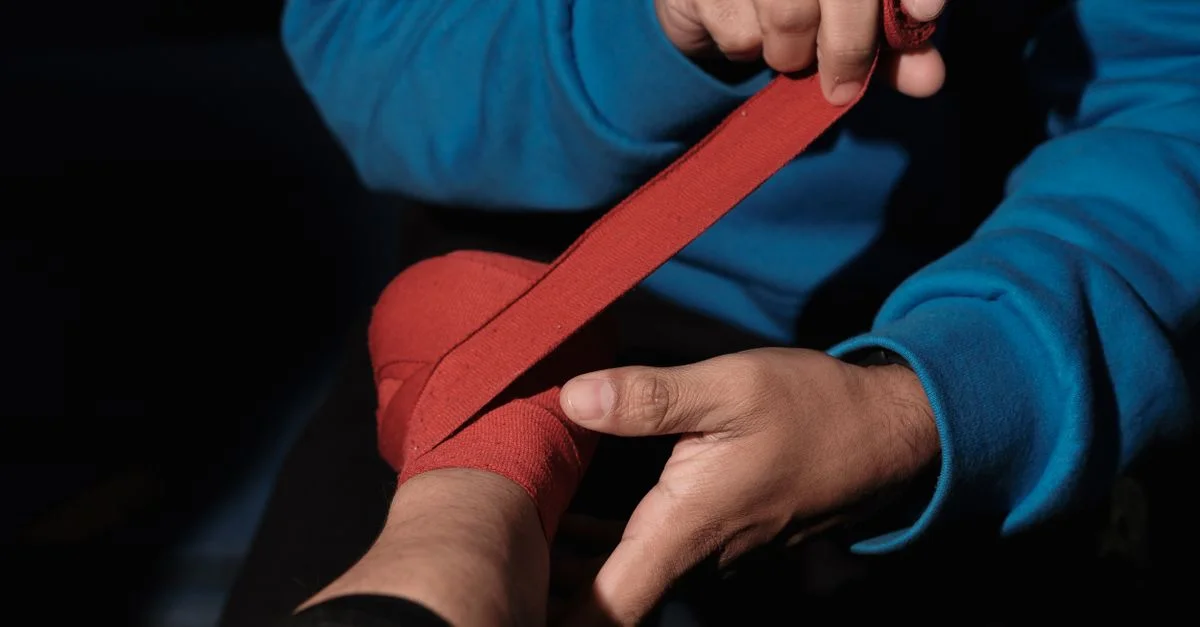 Gros plan sur des mains enroulant des bandages rouges, préparant une séance d'entraînement de boxe.
