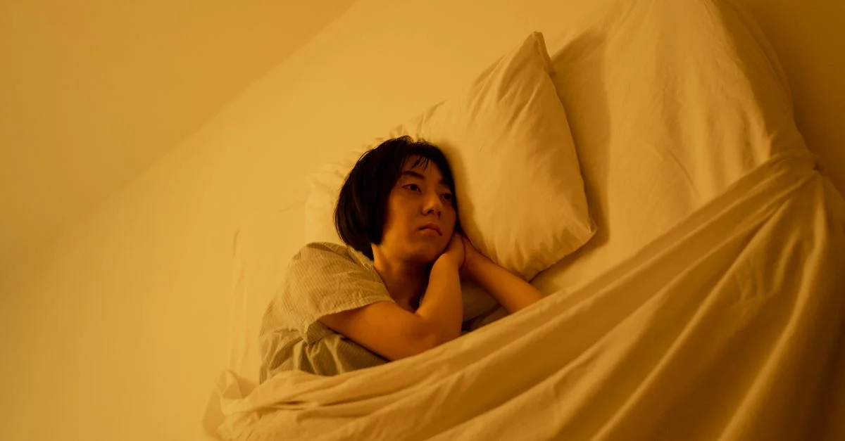 Une femme en pyjama est allongée sur un lit, reflétant ses émotions dans une chambre faiblement éclairée.