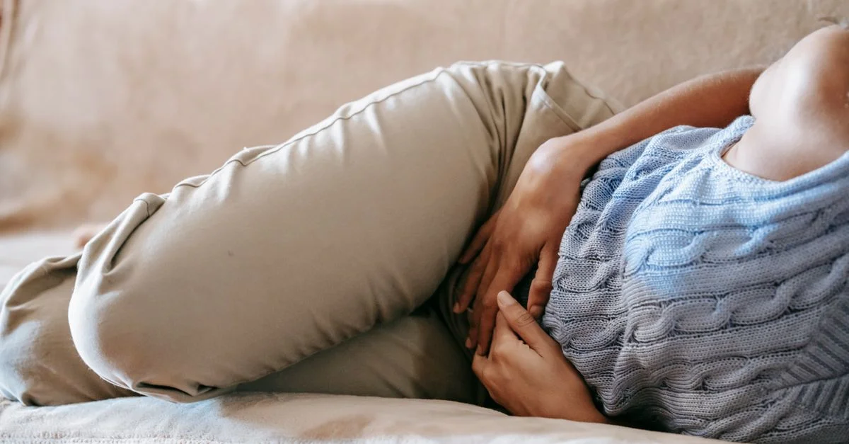 Une personne allongée sur un canapé tenant son ventre avec inconfort, symbolisant la douleur abdominale.