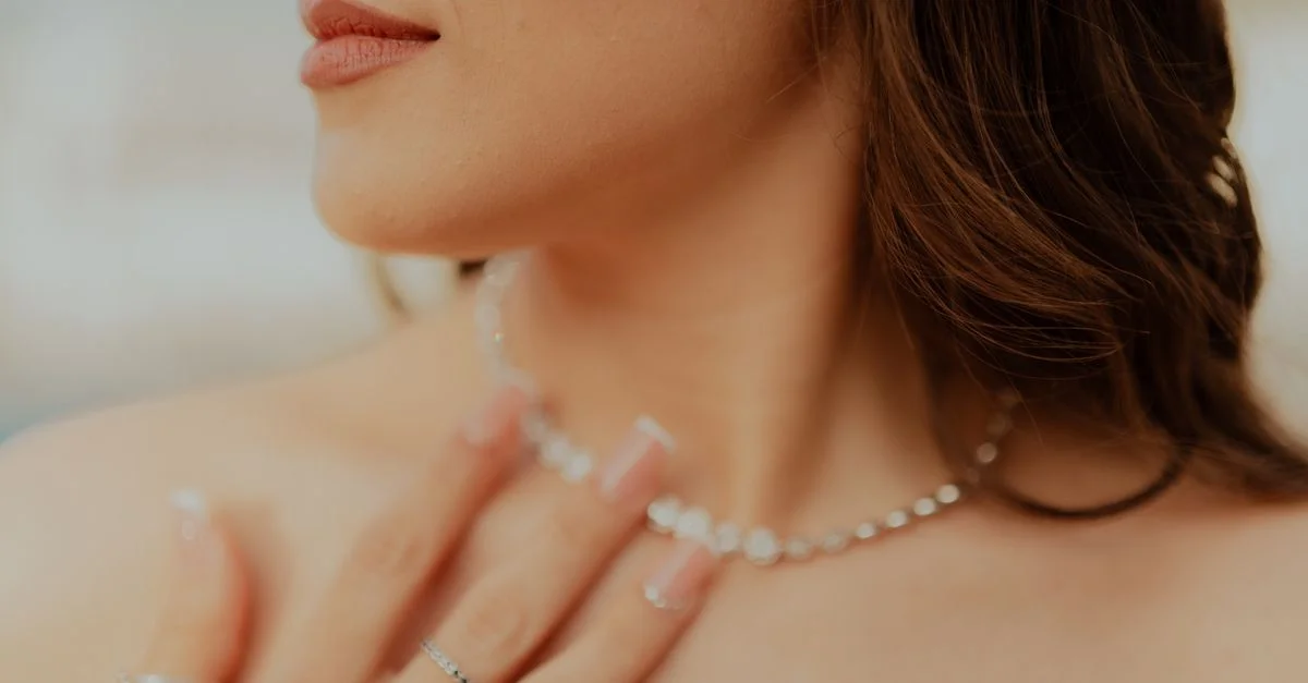 Gros plan d'une femme touchant son collier en diamants avec des ongles manucurés.