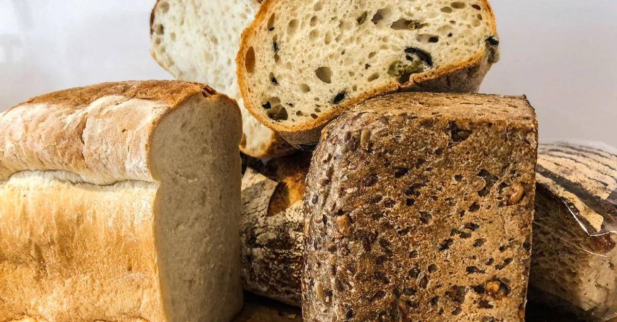 Gros plan sur divers pains artisanaux et tranches sur une planche en bois, mettant en avant des textures fraîches et cuites.