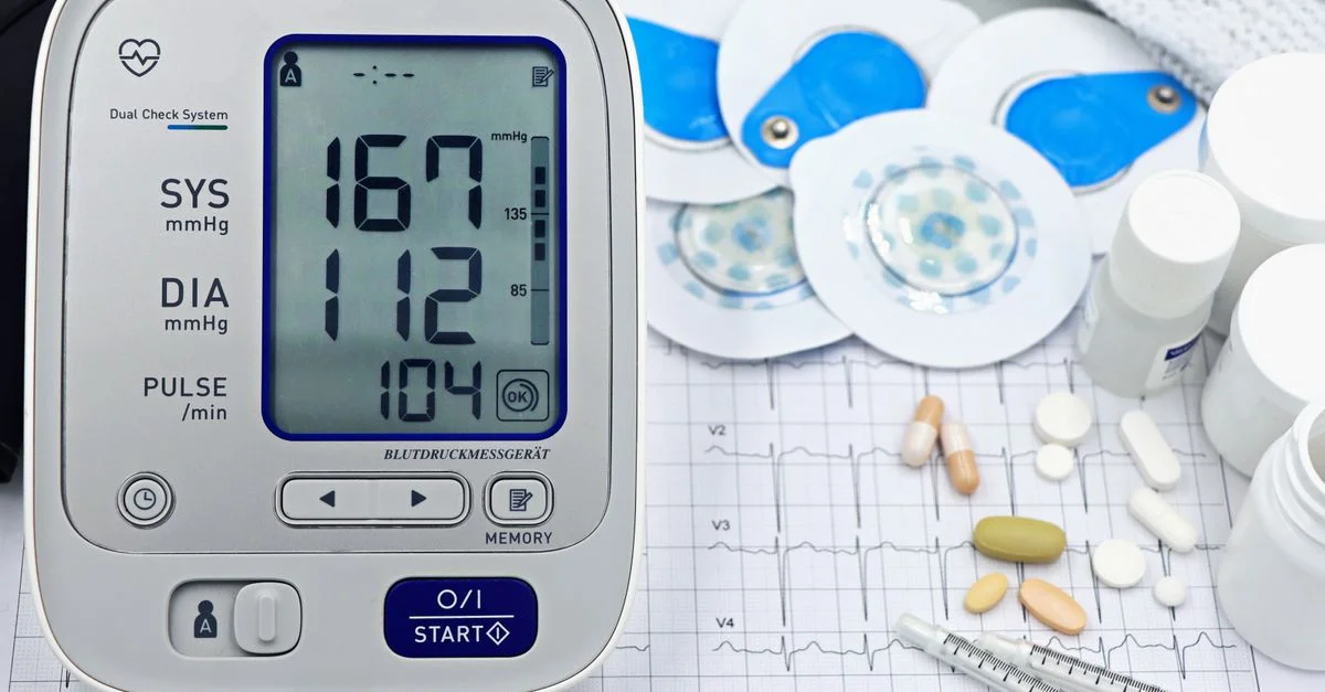 Gros plan d'un équipement médical comprenant un tensiomètre et des pilules sur un graphique ECG.