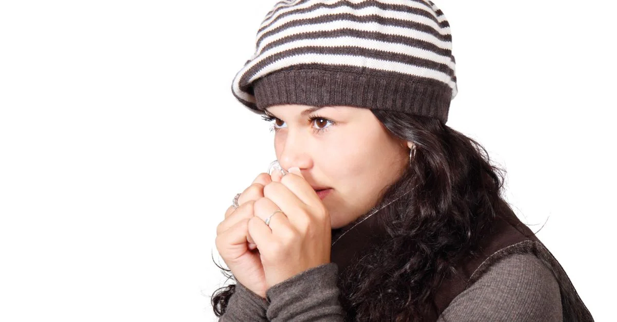 Une femme portant un bonnet rayé et des vêtements d'hiver, ayant l'air frigorifiée par un jour froid.