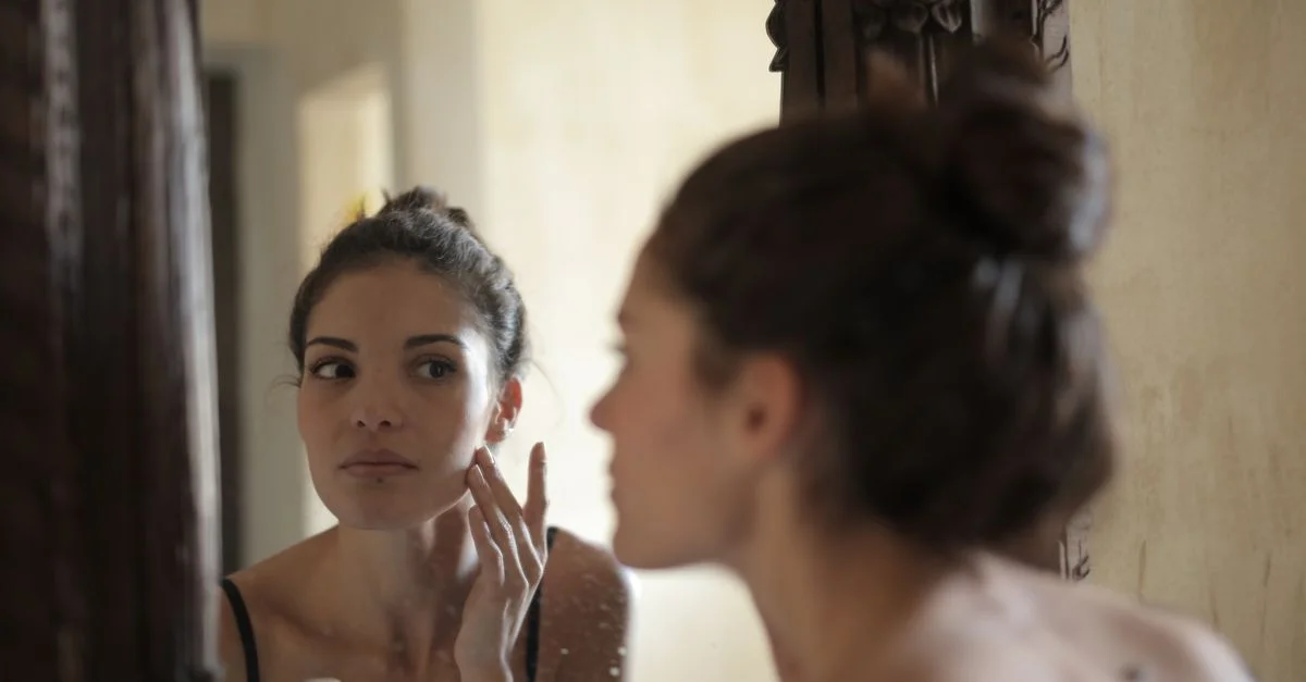 Une femme vérifie sa peau dans le miroir, engageant sa routine de soins de la peau du matin à l'intérieur.