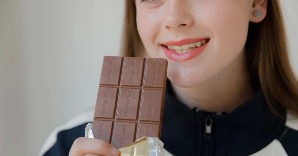 Femme souriante tenant une barre de chocolat, profitant de cette douceur.
