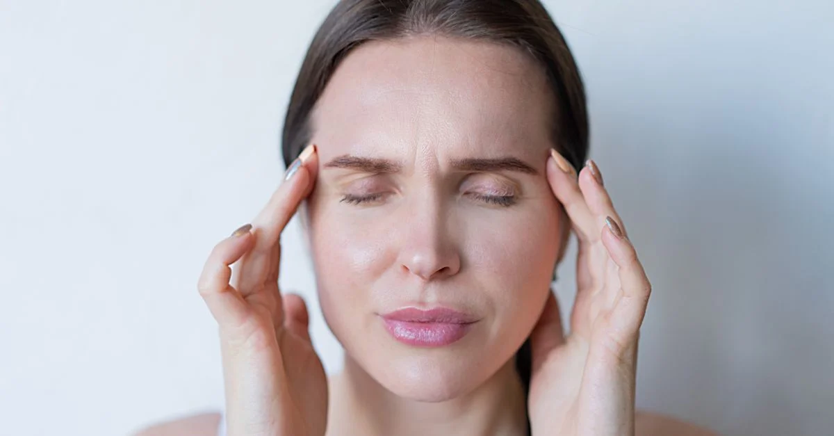Gros plan sur une femme les yeux fermés tenant ses tempes, montrant des signes de migraine ou de mal de tête.