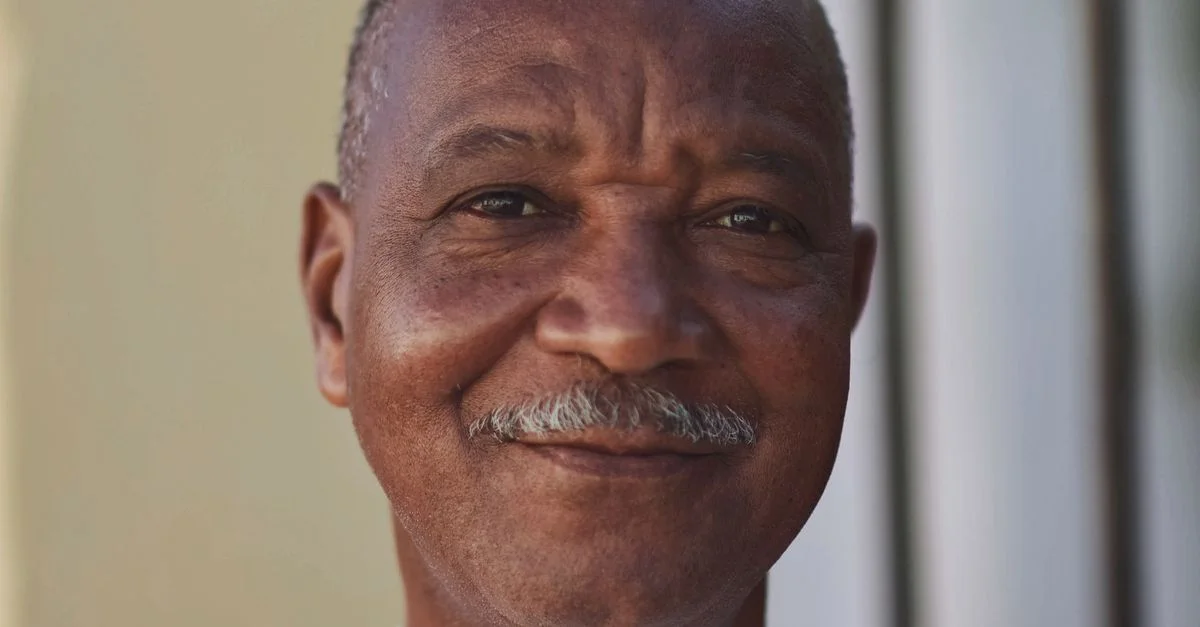Un portrait joyeux d'un homme africain âgé avec une moustache, profitant du soleil.