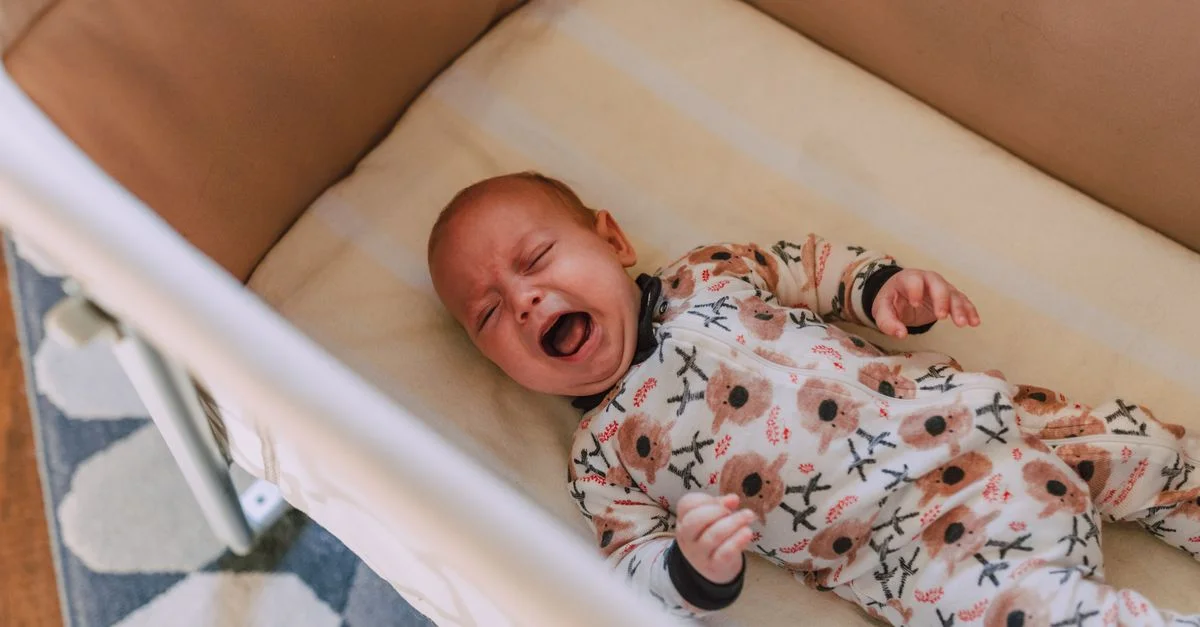 Un bébé mignon dans une grenouillère fleurie pleurant dans un berceau douillet, vu d'en haut.