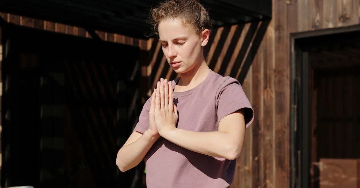 Jeune femme méditant en plein air avec les mains réunies en pose de namaste sous le soleil.