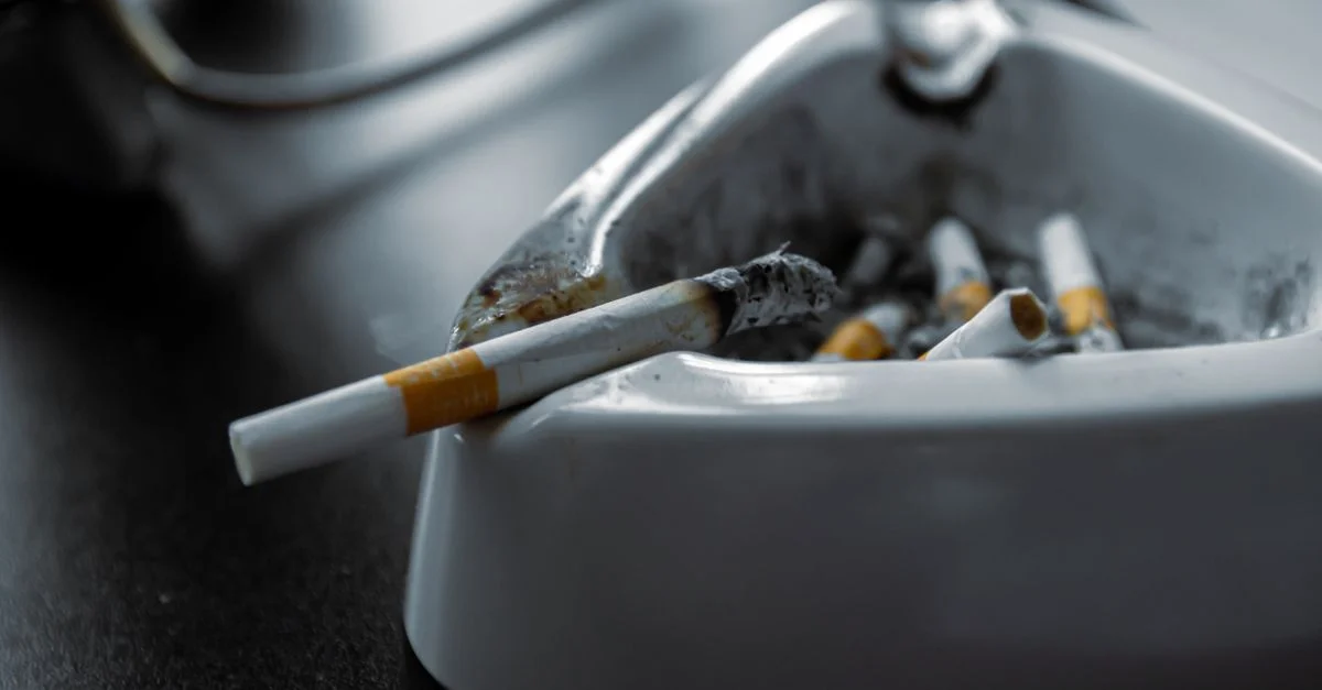 Une prise de vue en gros plan d'un cendrier blanc rempli de cigarettes usagées sur une surface sombre.