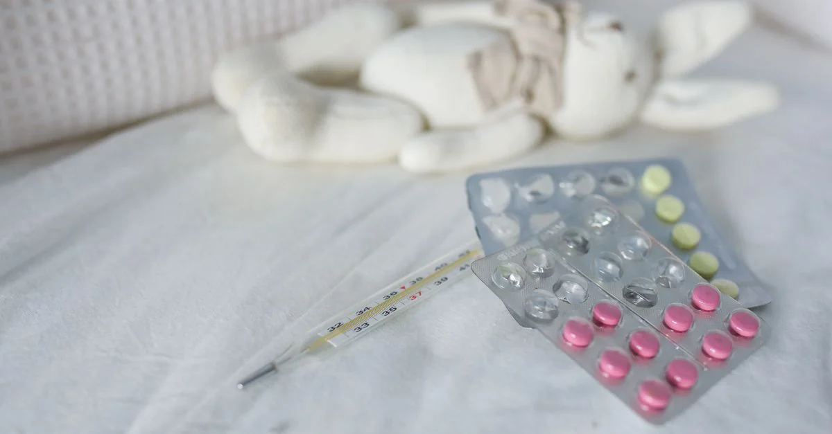 Gros plan sur des médicaments et un thermomètre sur un lit à côté d'un jouet lapin en peluche, symbolisant le soin des maladies infantiles.