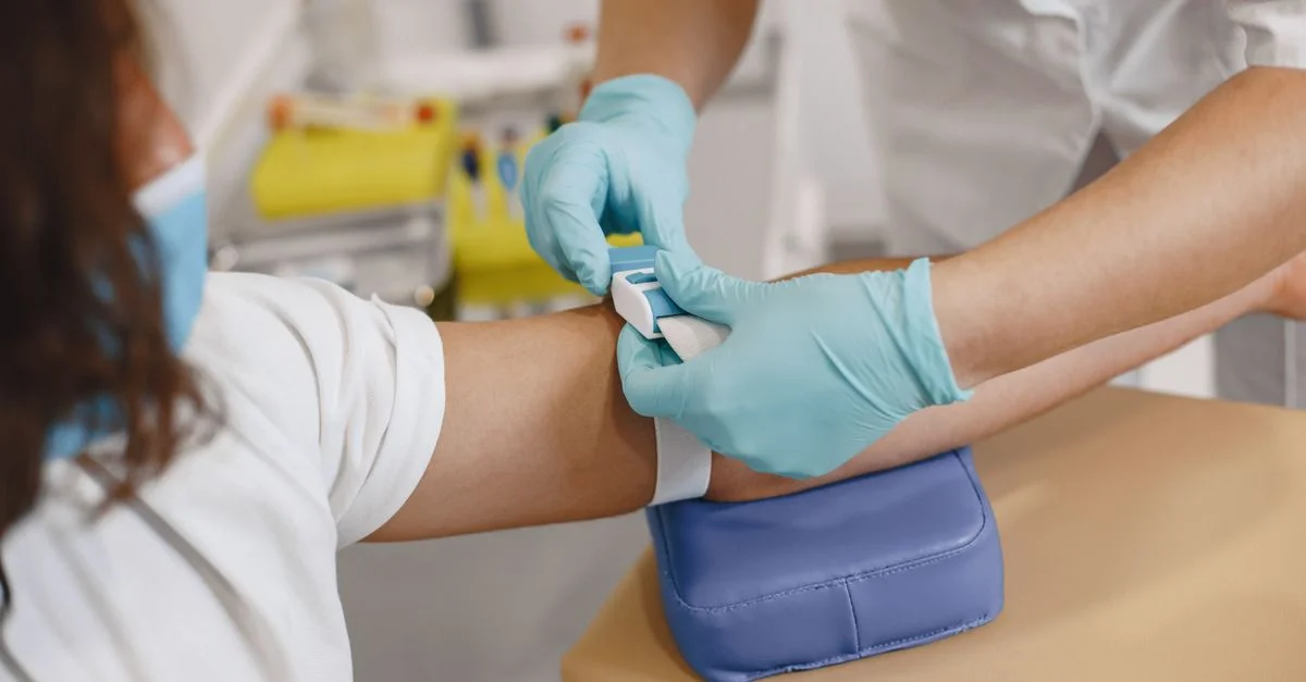Gros plan d'un professionnel de santé préparant le bras d'un patient pour une prise de sang dans un cadre clinique.