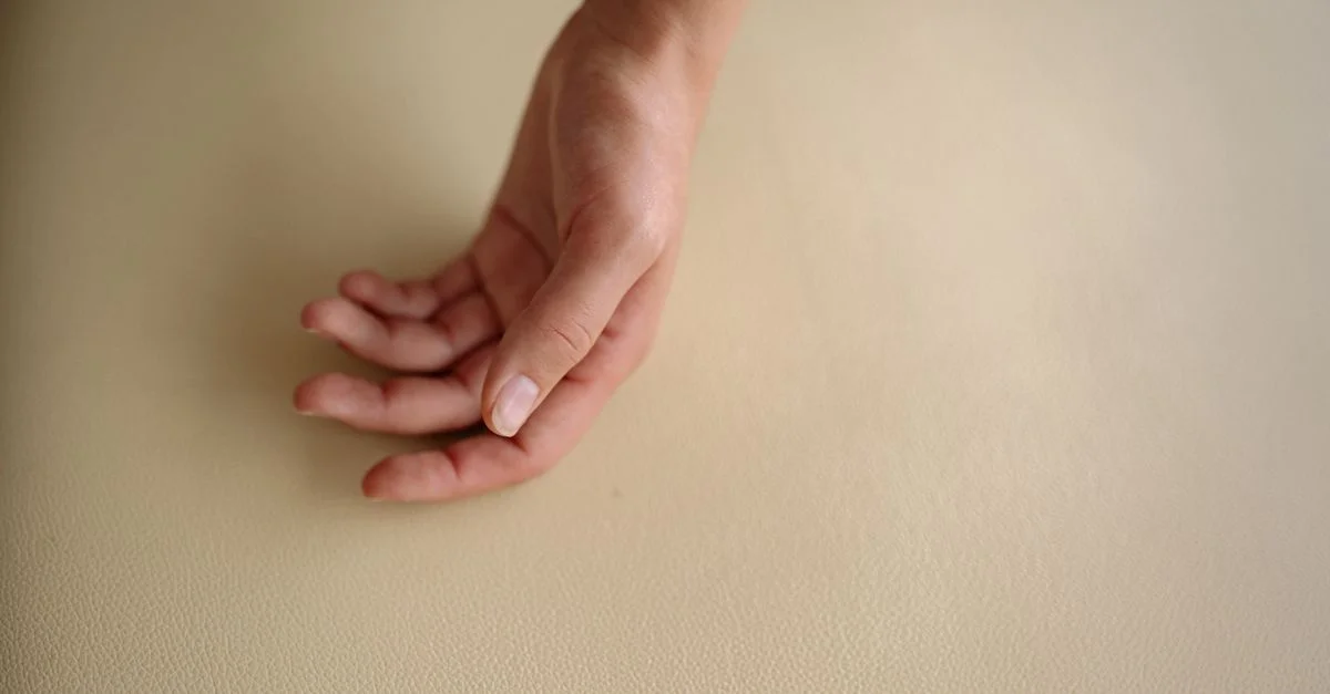 Une main détendue repose sur une surface en cuir texturé, capturant des détails subtils dans un style minimaliste.
