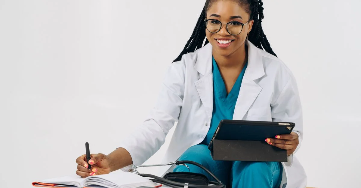 Médecin femme souriante en blouse avec une tablette et un stéthoscope, écrivant des notes.