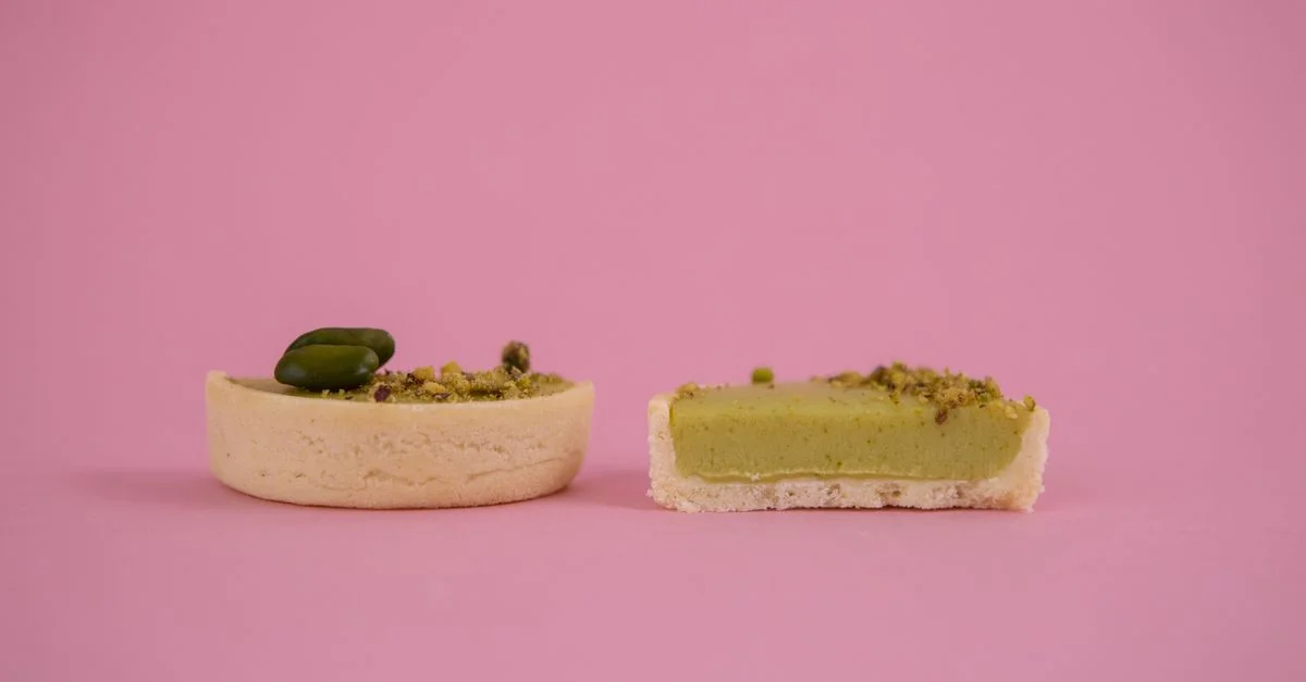 Gros plan d'élégantes tartelettes aux pistaches avec une garniture verte onctueuse sur un fond rose pastel.