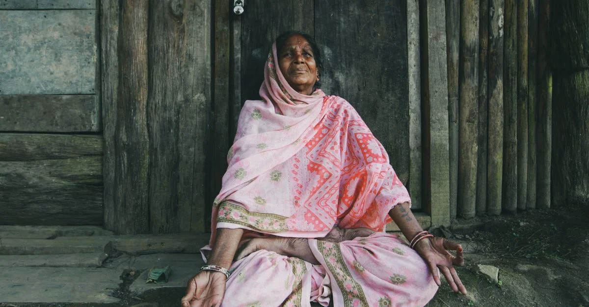 Portrait d'une femme âgée méditant en position tailleur dans un cadre de village.