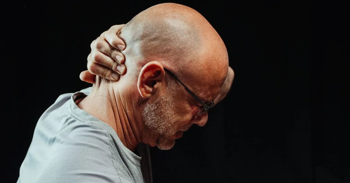 Vue de côté d'un homme se tenant le cou avec douleur sur fond noir.