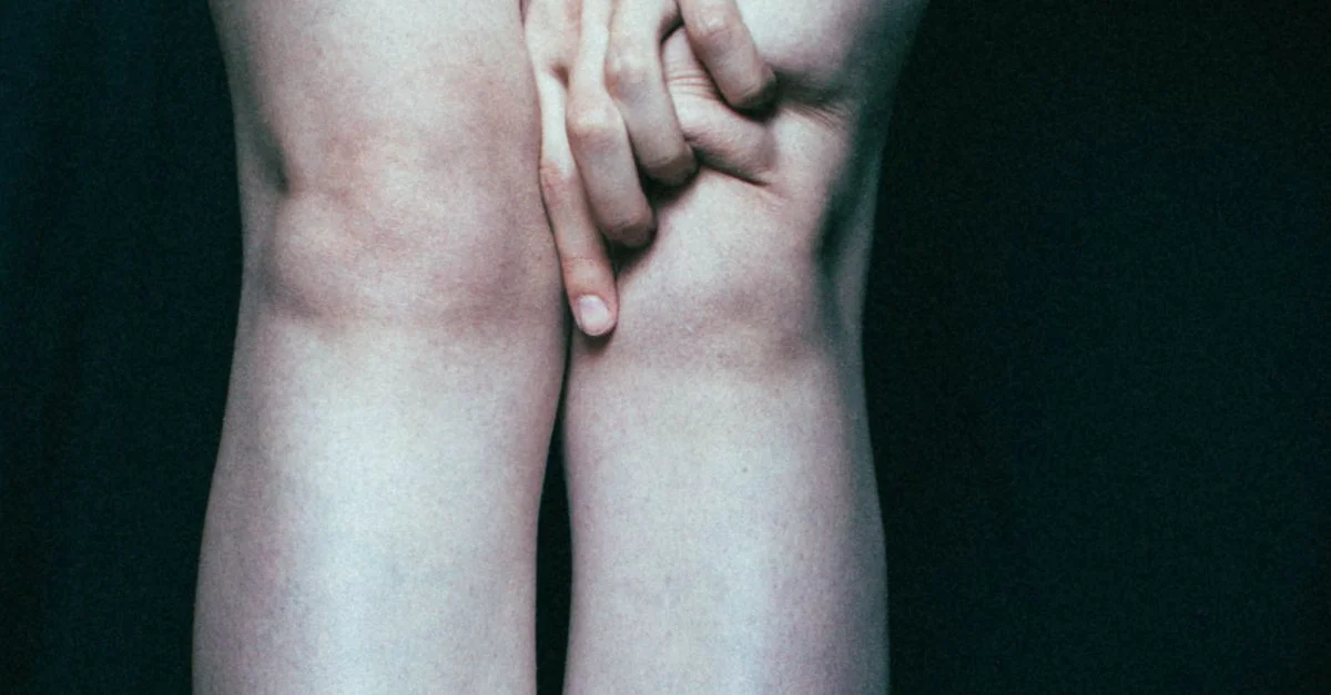 Gros plan artistique de mains humaines et de genoux avec un fond sombre, mettant en évidence la texture et la posture.