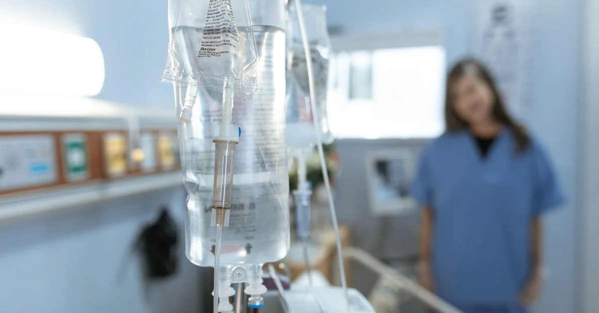 Gros plan d'une perfusion IV dans un hôpital avec une infirmière floue en arrière-plan.