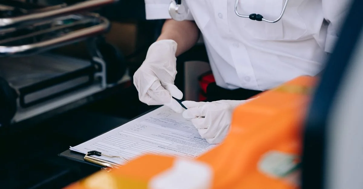 Un médecin portant des gants et un stéthoscope prend des notes à l'intérieur d'une ambulance.