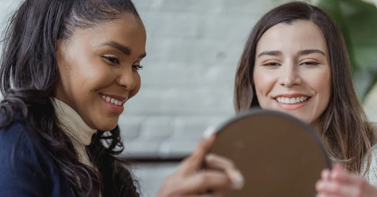 Deux femmes souriantes tenant un miroir à l'intérieur, montrant joie et beauté.