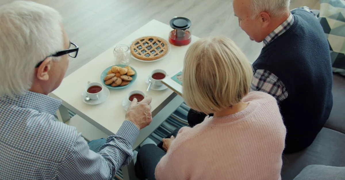 Des amis âgés se réunissent pour prendre le thé et manger des biscuits dans un cadre chaleureux.