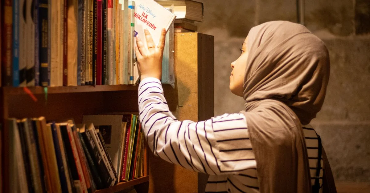Une femme avec un foulard explore les étagères de la bibliothèque, choisissant un livre à Kayseri, en Turquie.