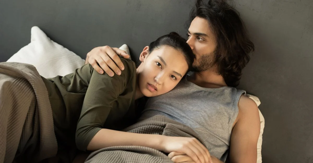 Couple romantique s'enlaçant dans un lit, montrant l'amour et la complicité dans un cadre confortable.