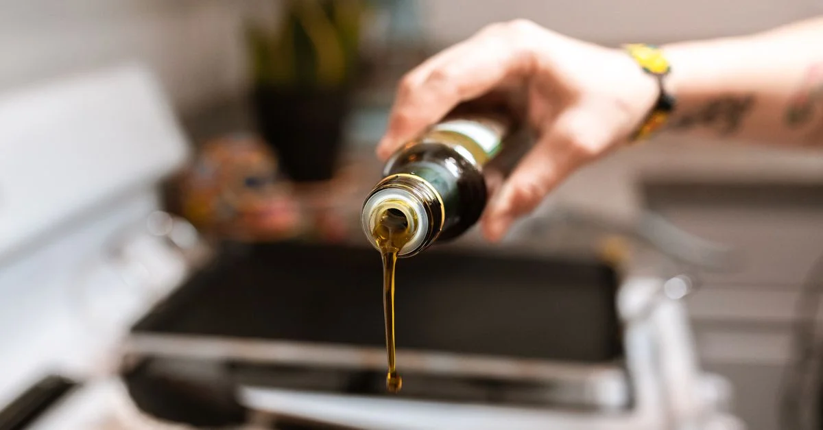 Une image centrée montrant de l'huile d'olive versée d'une bouteille dans une poêle pendant la cuisson.