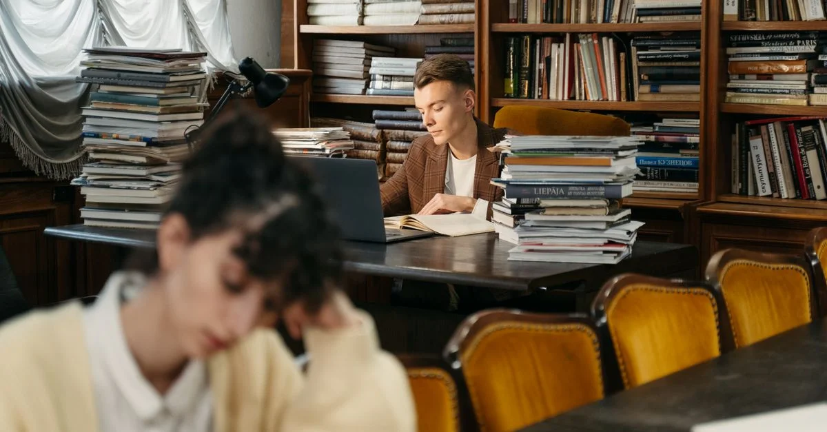 Un jeune homme concentré profondément en train de lire dans une bibliothèque confortable et bien fournie.
