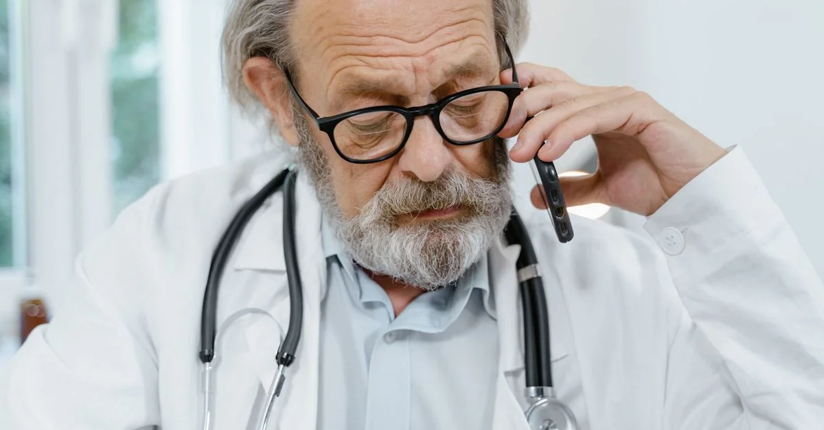Médecin âgé en blouse blanche et lunettes, parlant au téléphone, suggérant la télémédecine.