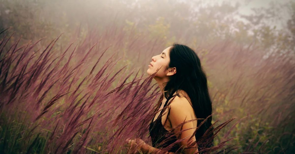 Une jeune femme sereine, les yeux fermés, profitant d'une prairie couverte de brume, immergée dans la nature.