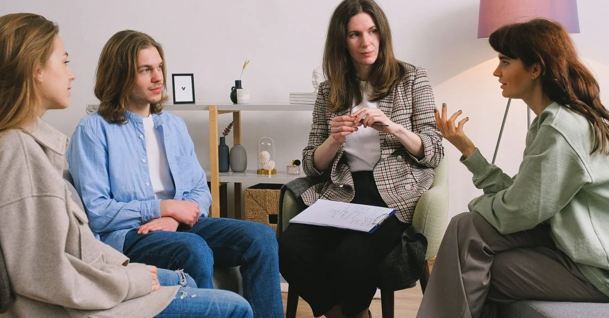 Une séance de thérapie de groupe se déroulant à l'intérieur avec un conseiller attentif guidant la discussion.