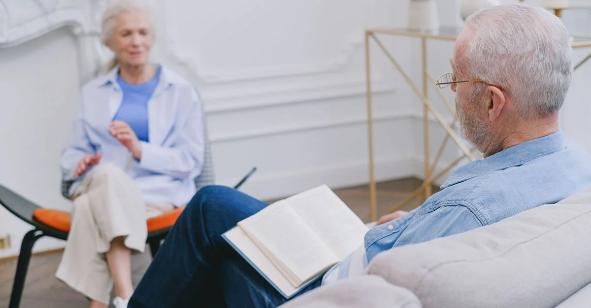 Des personnes âgées assises sur un canapé, profitant d'un moment paisible avec un livre et une conversation.