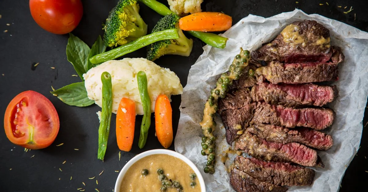 Steak grillé accompagné de légumes frais et de sauce au poivre, présentant un repas coloré et appétissant.
