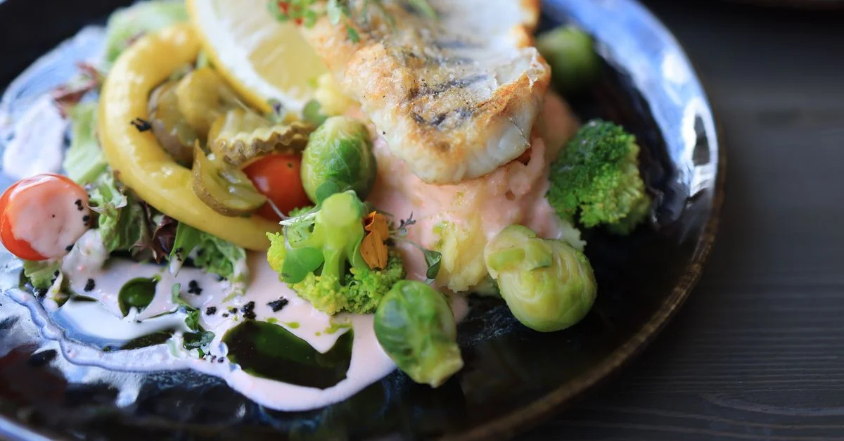 Gros plan d'un plat de poisson gastronomique avec des légumes variés sur une assiette sombre.
