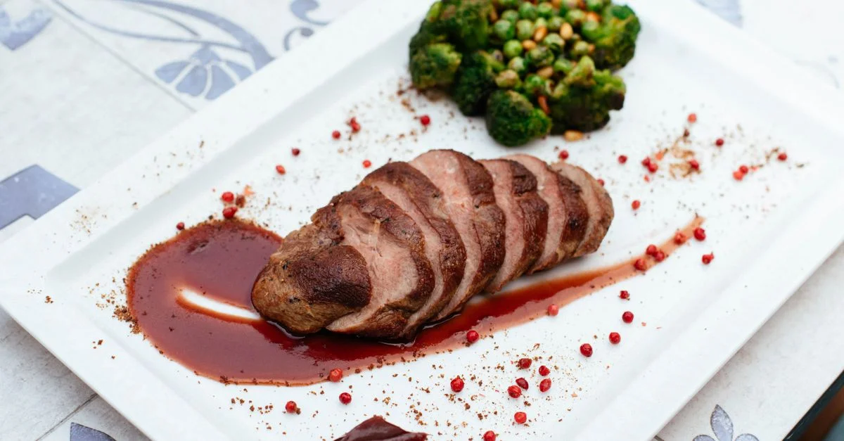 Magret de canard délicieusement dressé avec brocoli et sauce sur une assiette blanche.