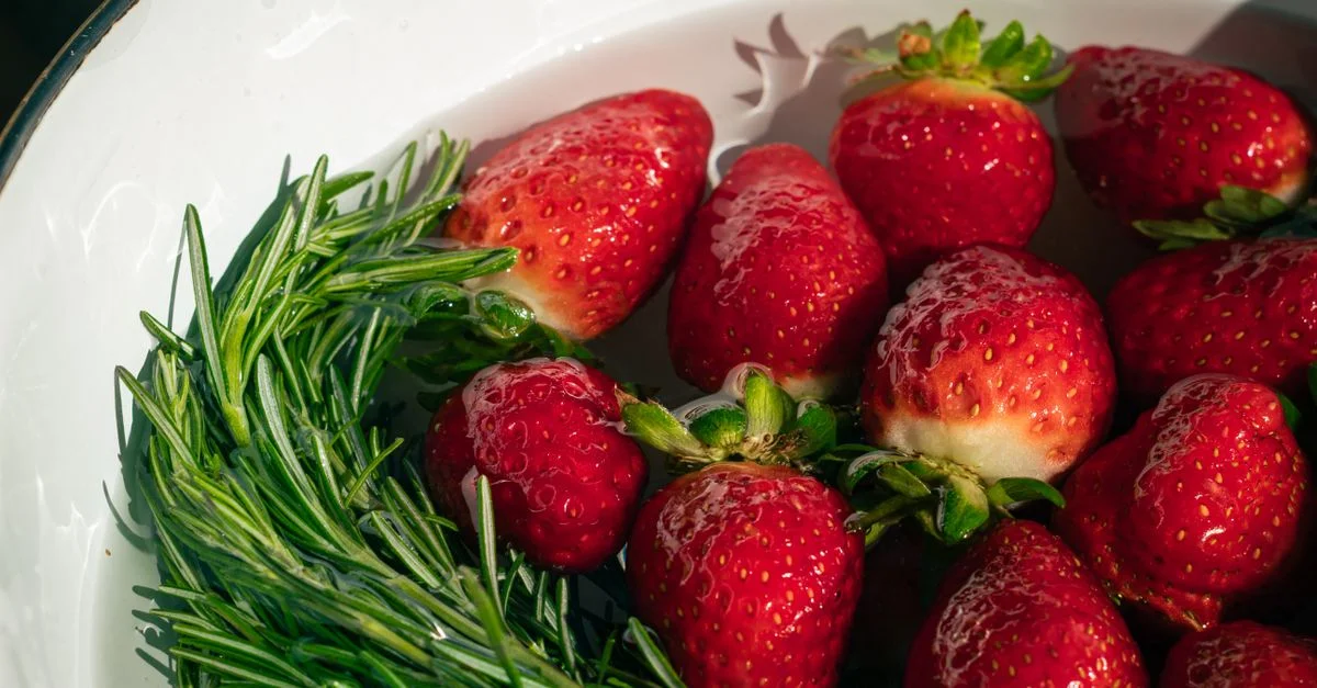 Gros plan sur des fraises fraîches et du romarin dans un bol, illuminés par la lumière naturelle.