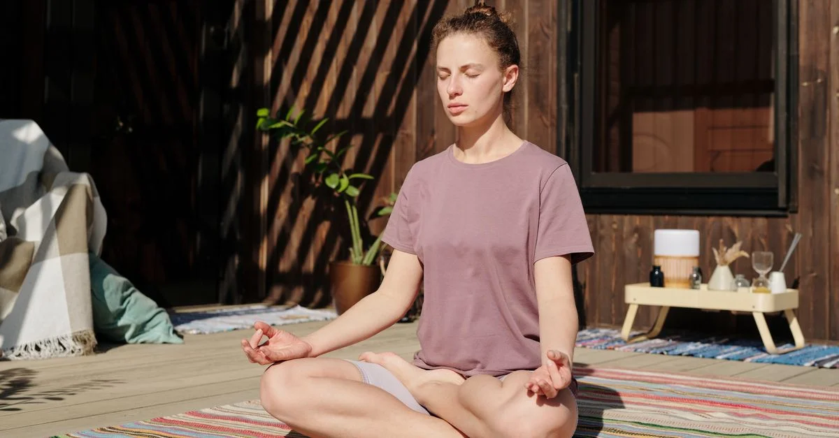Femme pratiquant la méditation en pose de lotus sur une terrasse ensoleillée.