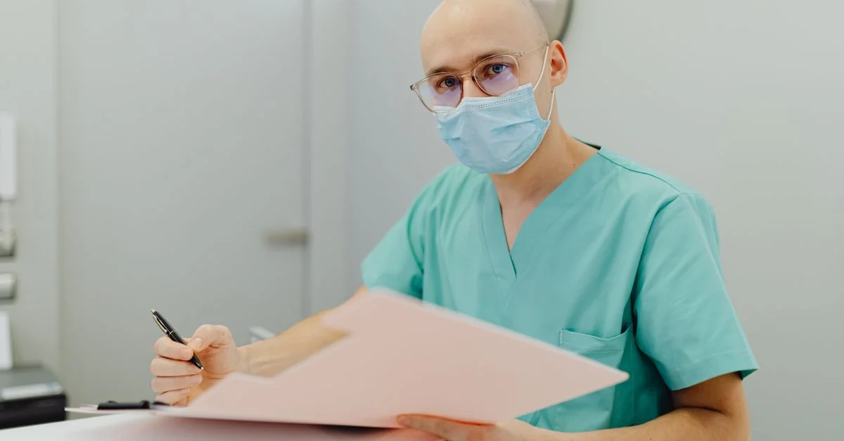 Professionnel médical en tenue de travail avec masque, se concentrant sur la documentation des soins aux patients.