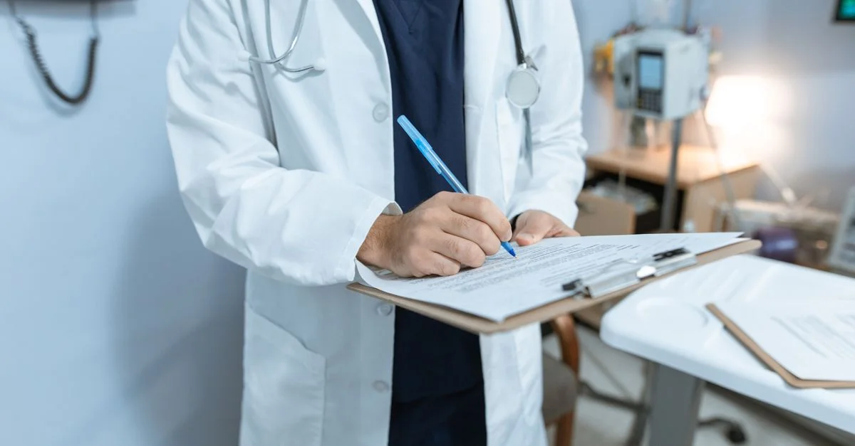 Un médecin en blouse blanche prenant des notes dans un hôpital, à l'aide d'une planche à clips.