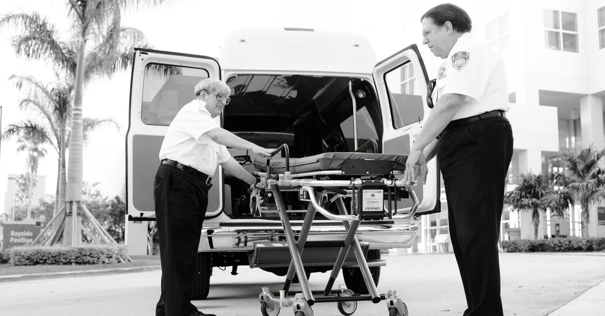Deux paramédics organisent une civière devant une ambulance, prêts pour un appel d'urgence.