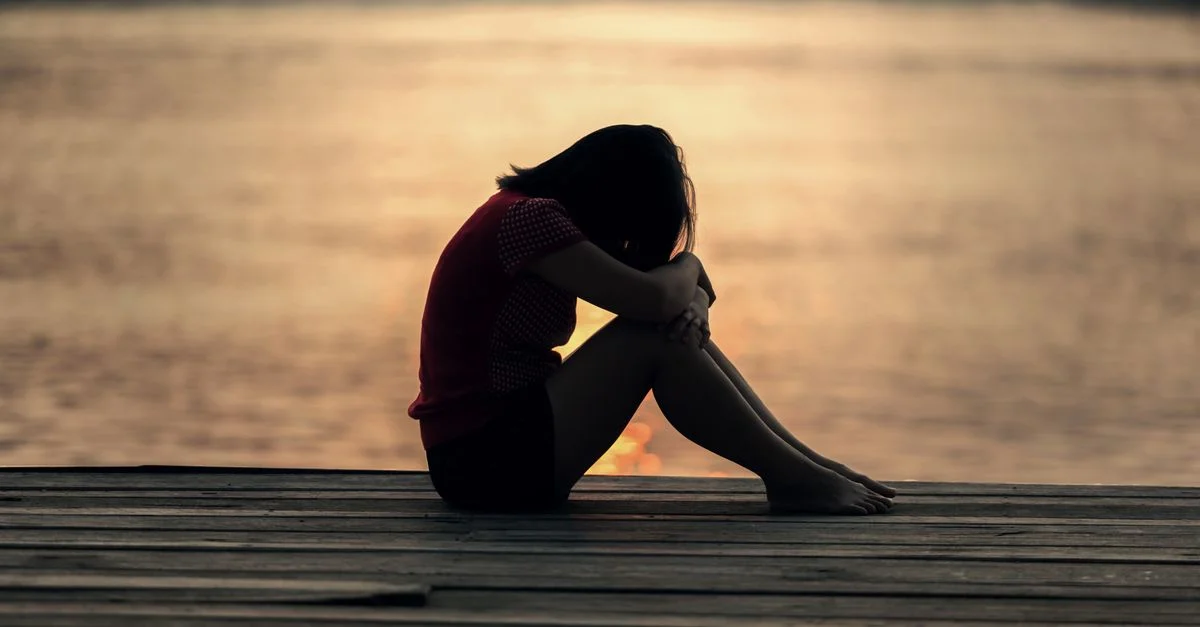 Une femme assise seule sur une jetée en bois au bord du lac, montrant solitude et réflexion.